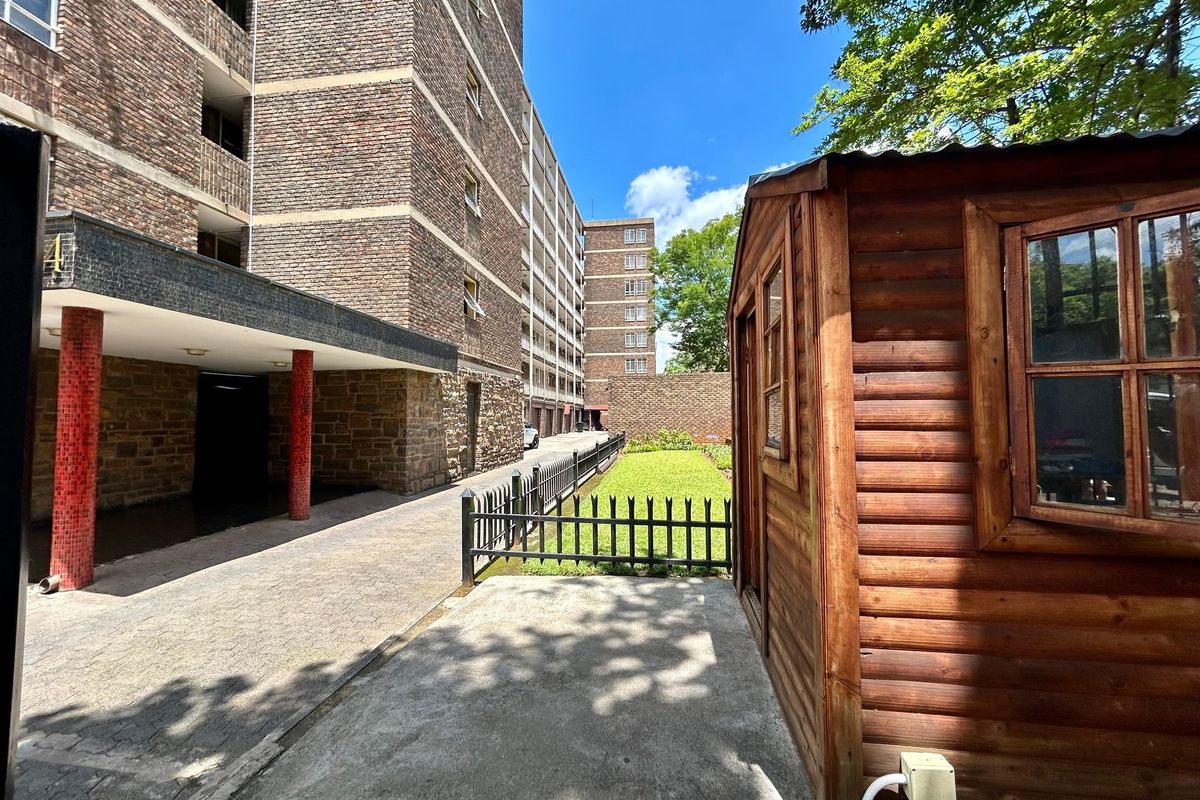 Rear exterior view of the apartment building featuring a paved driveway, small lawn area, and a wooden storage shed.