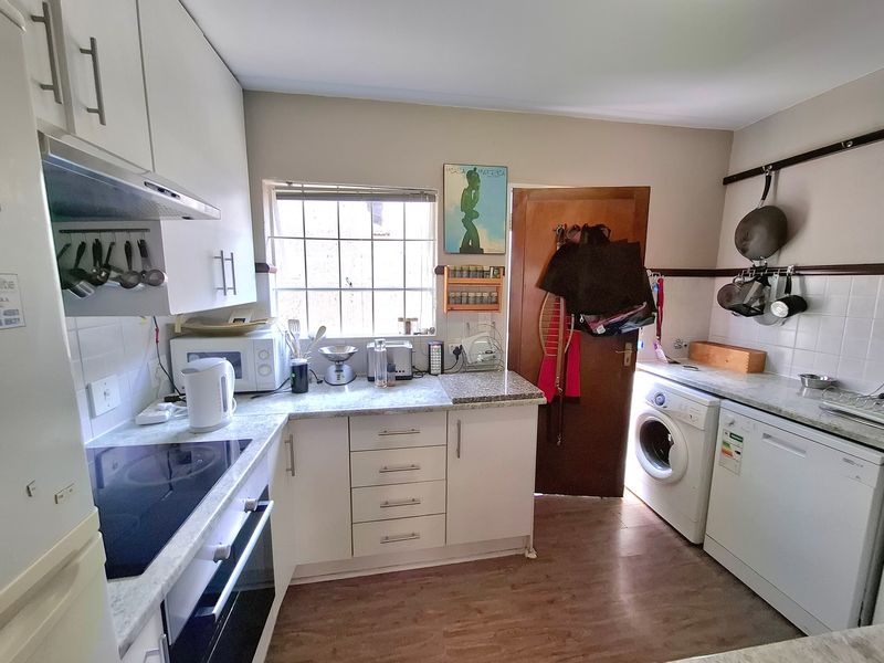 Functional kitchen featuring white cabinetry, laminate countertops, built-in oven, electric hob, and dedicated spaces for laundry and dishwasher appliances.