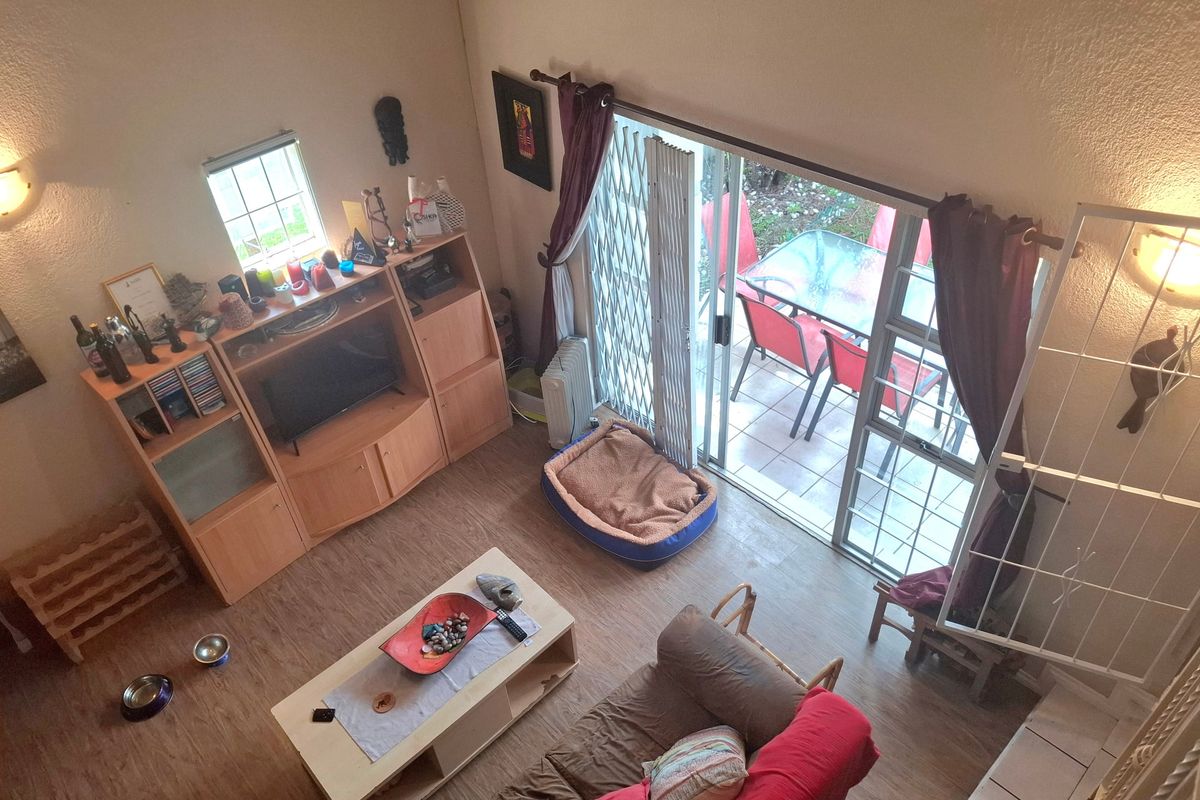 A high-angle view of a living room featuring laminate flooring, wall sconce lighting, and a sliding glass door leading to an outdoor patio area.