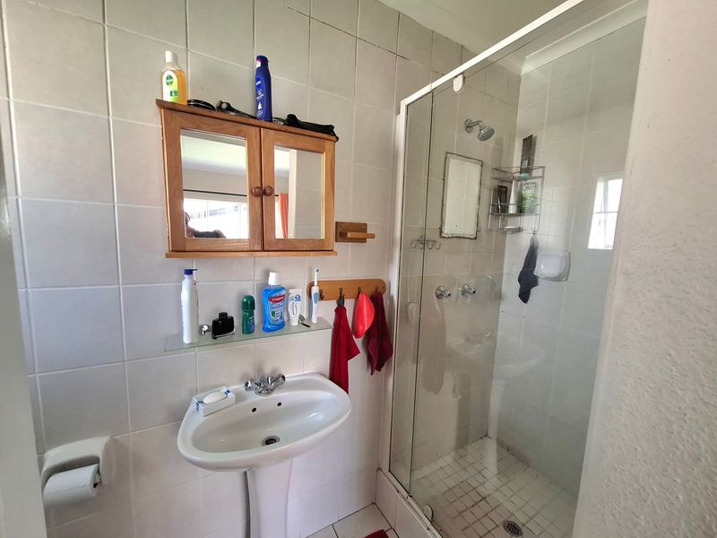 A functional bathroom featuring a pedestal basin, a glass-enclosed shower, and wall-mounted storage cabinetry with tiled finishes.