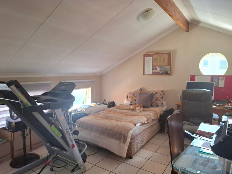 A bedroom featuring a sloped ceiling with an exposed timber beam, tiled flooring, and a unique circular window.