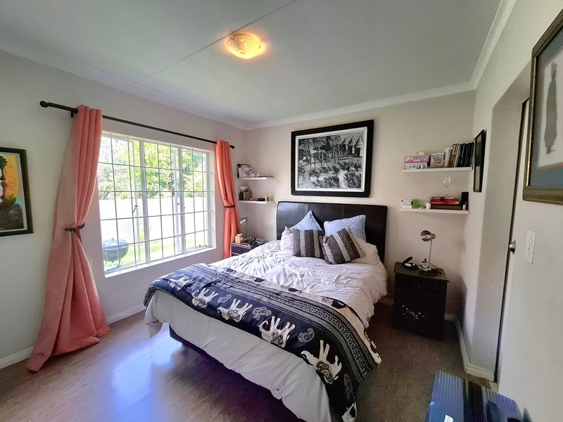 A well-lit bedroom featuring laminate flooring, a large window providing natural light, and built-in floating shelves for storage.