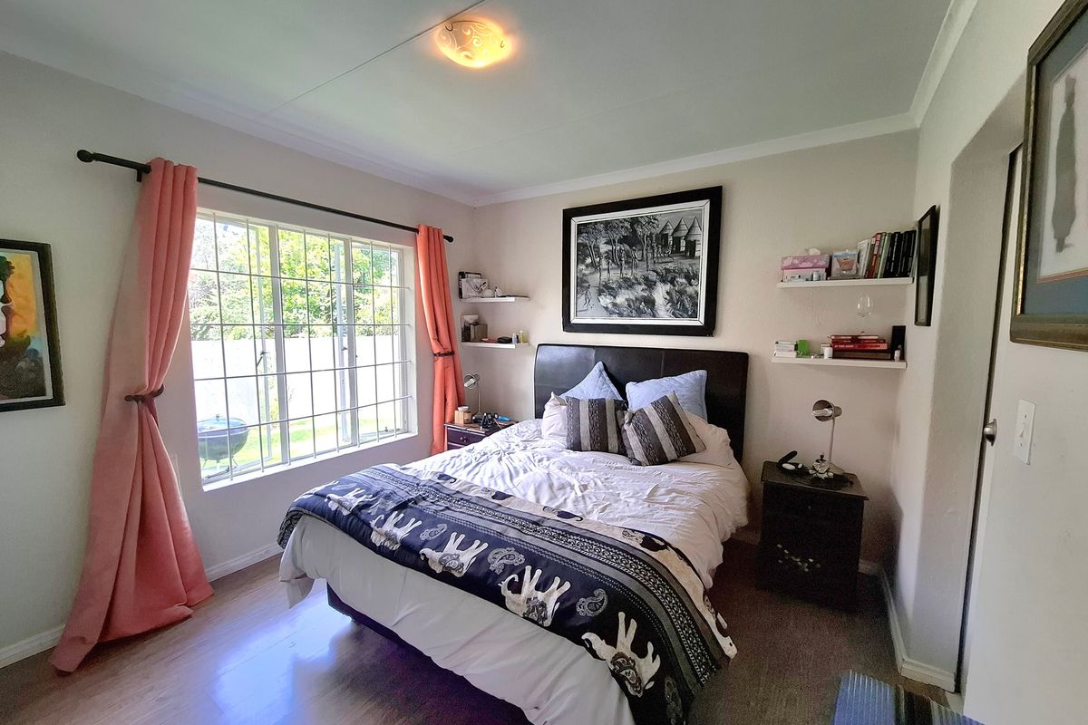 A well-lit bedroom featuring laminate flooring, a large window providing natural light, and built-in floating shelves for storage.