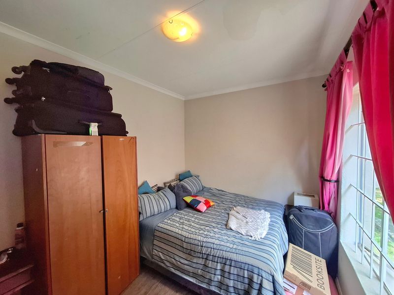 A functional bedroom featuring a built-in wardrobe and large window with security bars, offering a practical space for rest.