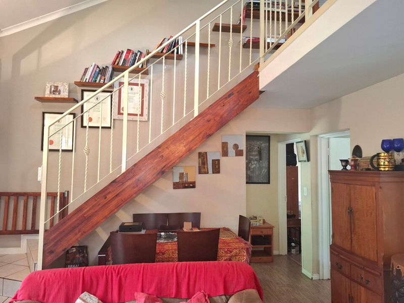 Open plan living area featuring a prominent timber staircase with metal balustrade and integrated wall shelving, leading to an upper level.