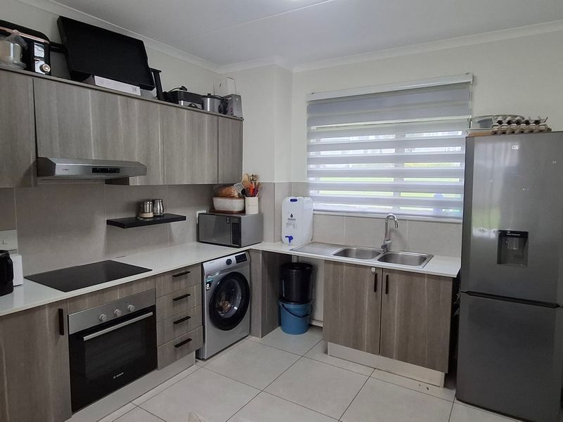 Modern kitchen featuring wood-grain cabinetry, integrated electric hob and oven, double sink, and tiled flooring with ample storage space.