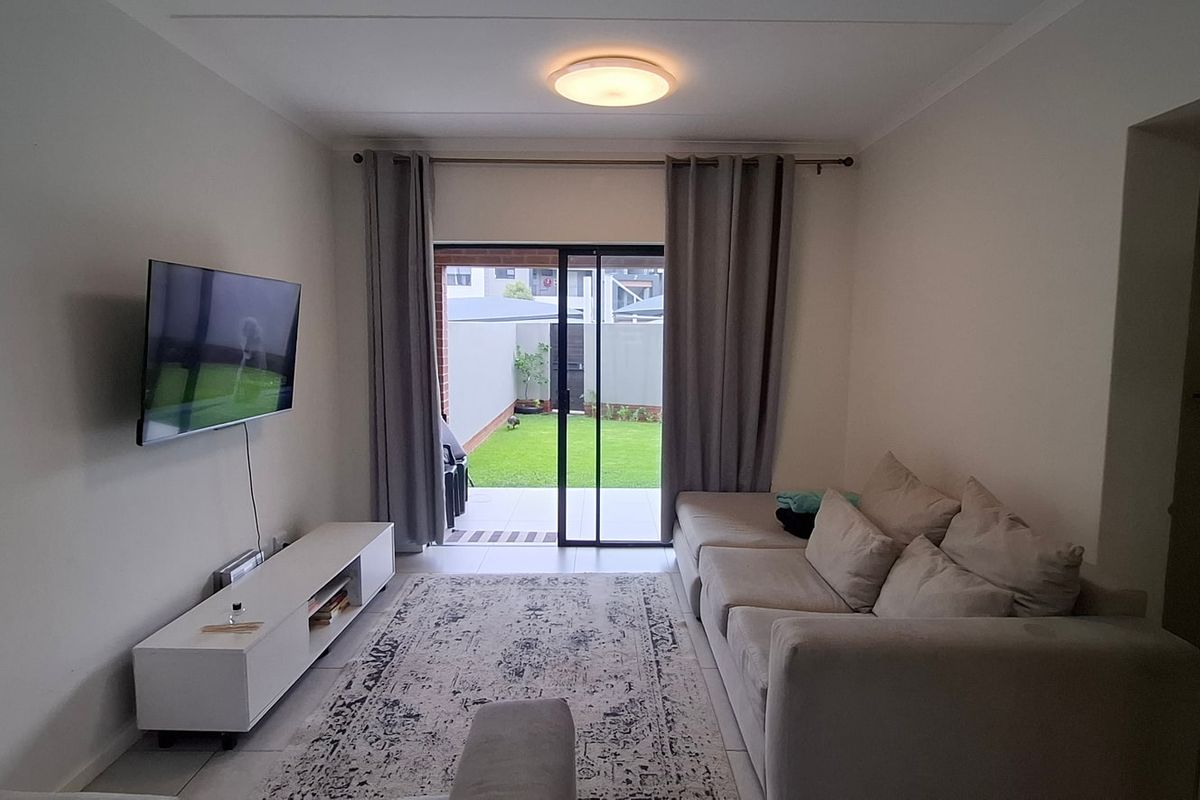 A well-maintained living room featuring tiled flooring and a sliding glass door that provides direct access to the rear garden area.