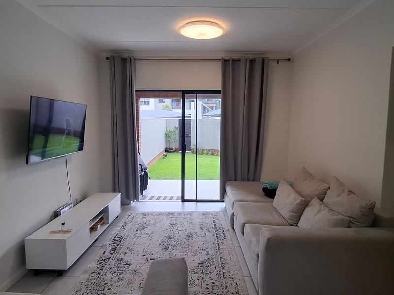 A well-maintained living room featuring tiled flooring and a sliding glass door that provides direct access to the rear garden area.