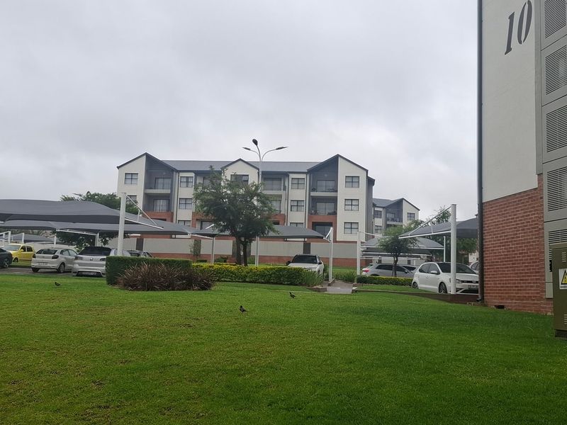 Exterior view of the apartment complex featuring landscaped grounds, covered parking bays, and brick building facade.
