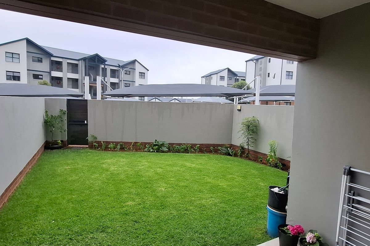 A private rear garden featuring a well-maintained lawn, enclosed by boundary walls, viewed from a covered patio area.