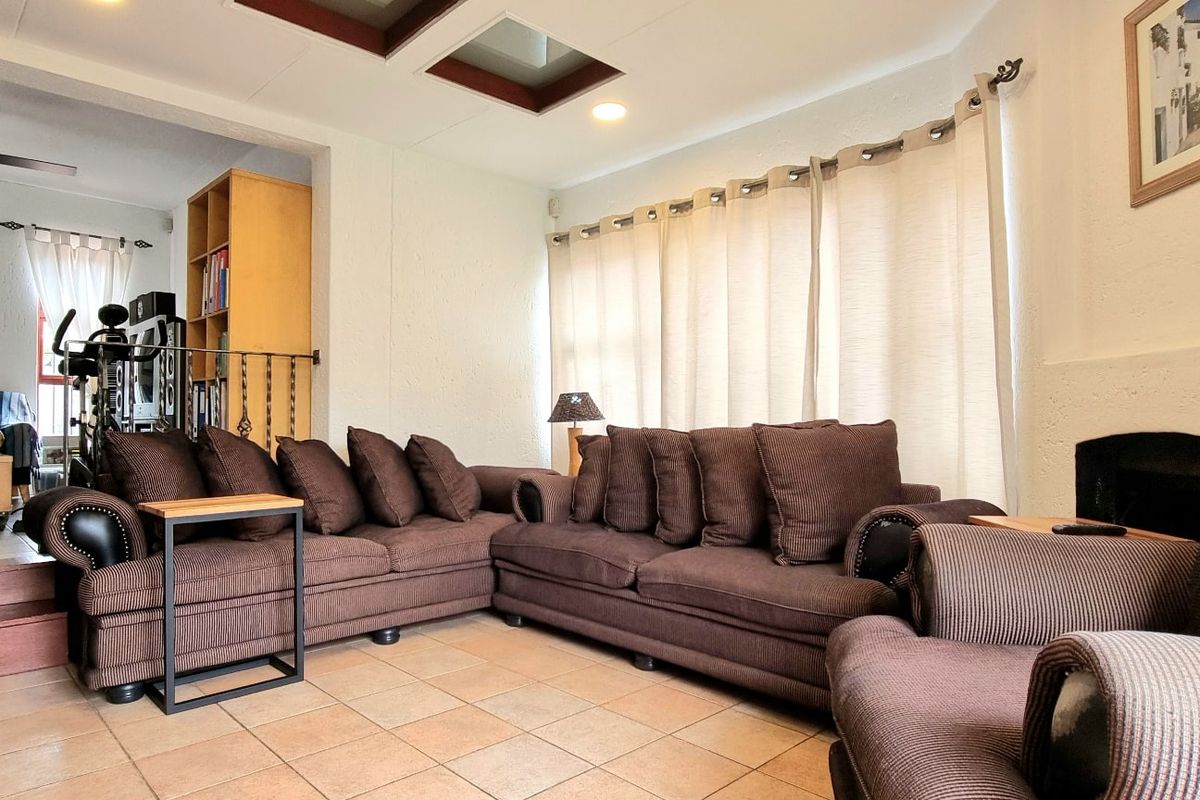 Spacious living room featuring tiled flooring, a built-in fireplace, a ceiling fan, and a skylight, with a stepped transition to an adjacent area.
