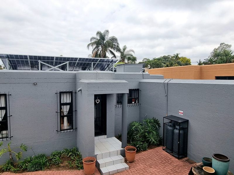 Front elevation of a cluster home featuring a grey painted facade, solar panel installation on the roof, and a paved entrance area.