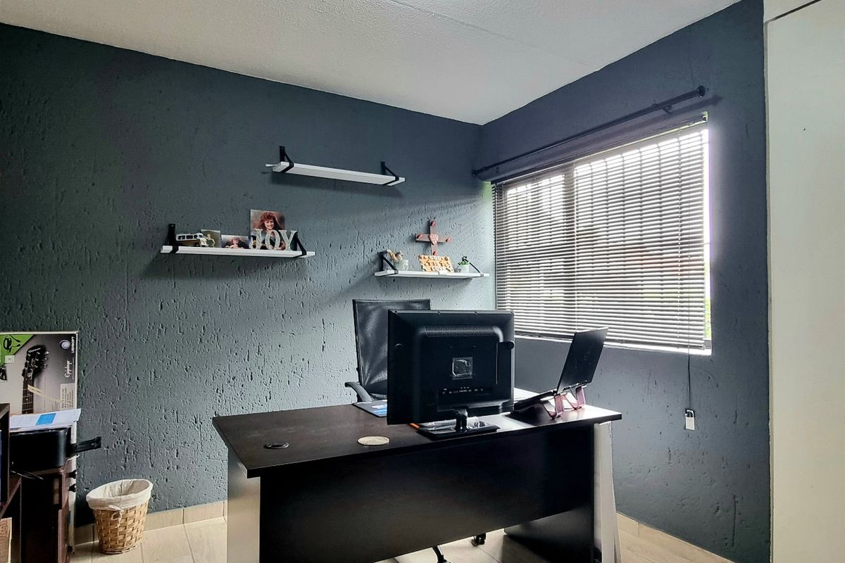 A bedroom currently utilized as a home office, featuring dark textured walls, tiled flooring, and a built-in cupboard.