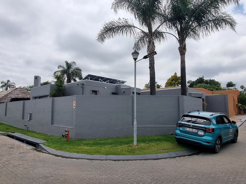 Corner view of a cluster property featuring a grey perimeter wall, solar panels on the roof, and a paved driveway.