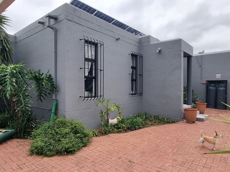 Rear exterior view of the property featuring a paved patio area, security bars on windows, and roof-mounted solar panels.
