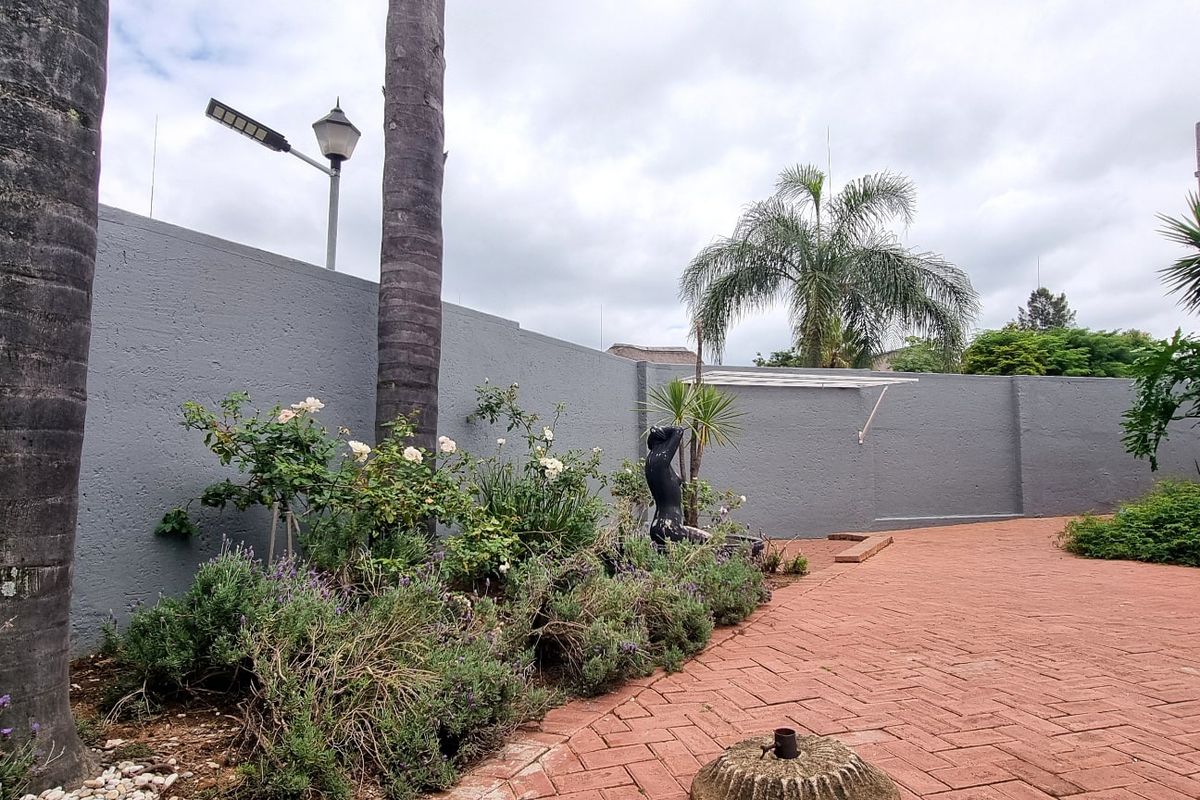 A private rear courtyard featuring durable brick paving, a high perimeter wall for privacy, and established garden beds with mature trees.