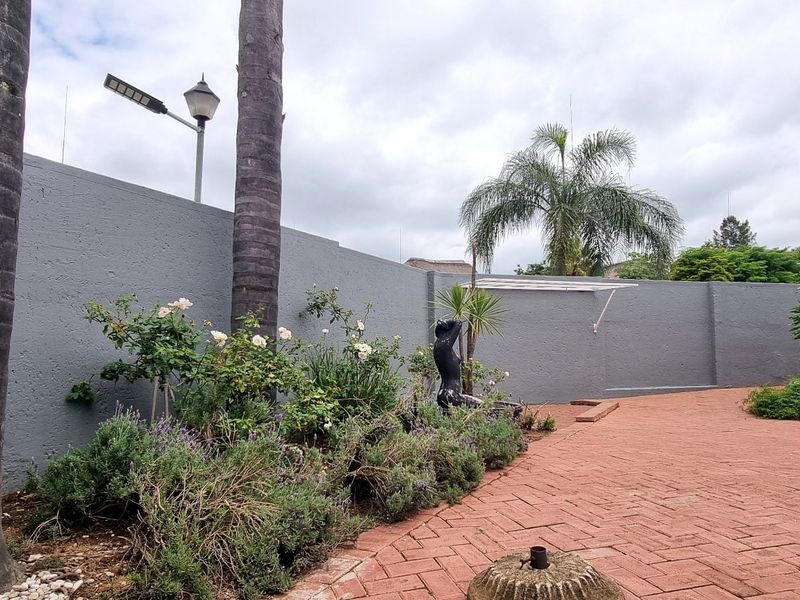 A private rear courtyard featuring durable brick paving, a high perimeter wall for privacy, and established garden beds with mature trees.
