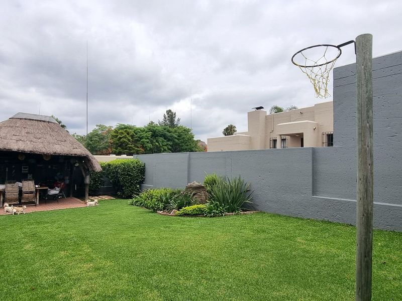 A private rear garden featuring a lawn, perimeter wall, and a traditional thatched lapa entertainment area.