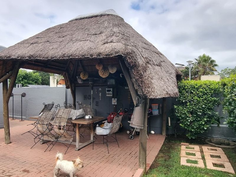Outdoor entertainment area featuring a traditional thatched lapa structure set on brick paving, providing a shaded space for outdoor dining and relaxation.