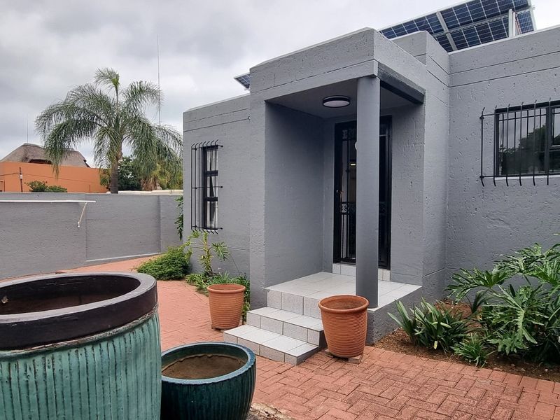 Front entrance area of a cluster home featuring a paved courtyard, security bars on windows, and roof-mounted solar panels.