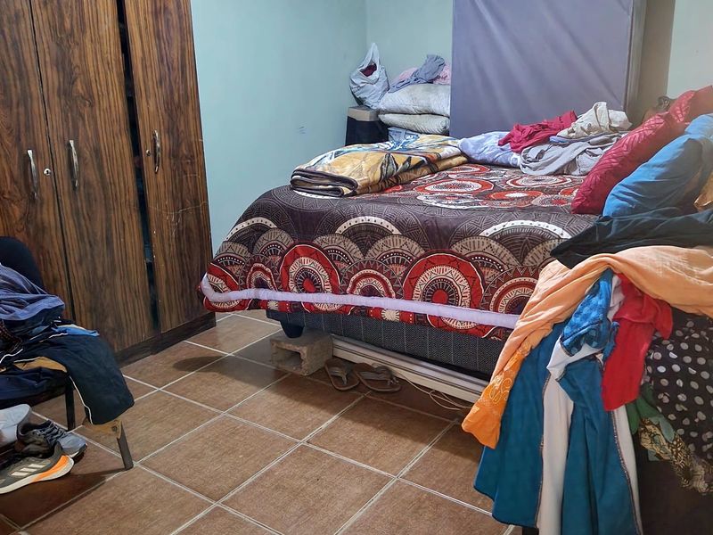 A bedroom featuring tiled flooring, a built-in wardrobe, and decorative ceiling cornicing, currently requiring cosmetic updates and maintenance to the walls and ceiling.
