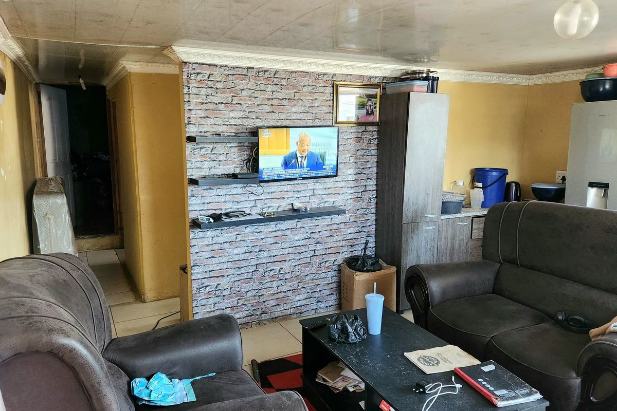A living room featuring a brick-effect accent wall with floating shelves, tiled flooring, and decorative ceiling coving.