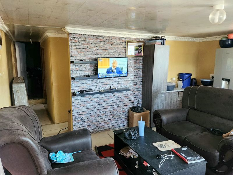 A living room featuring a brick-effect accent wall with floating shelves, tiled flooring, and decorative ceiling coving.