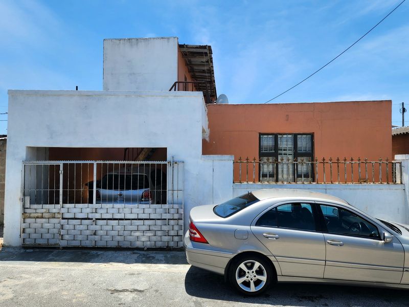 Front elevation of a residential property featuring a gated carport, security fencing, and exterior masonry requiring maintenance and repainting.