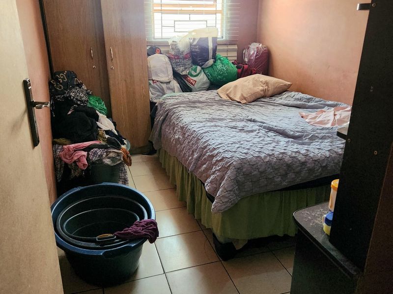 A compact bedroom featuring tiled flooring and a window with blinds, currently requiring cosmetic updates to the wall and ceiling finishes.