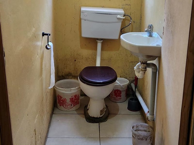 A small, dated guest bathroom featuring a toilet, wall-mounted basin, and tiled flooring, currently in need of cosmetic renovation and wall repairs.