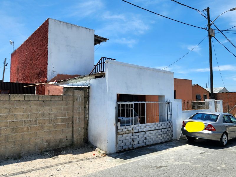 Front exterior view of a residential property featuring a metal security gate, concrete boundary wall, and a multi-level structure with visible exterior wear.