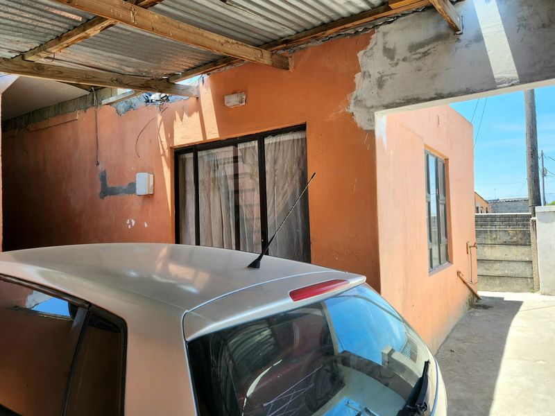 Rear exterior view showing a covered patio area with unfinished wall plaster and exposed timber roof structure.