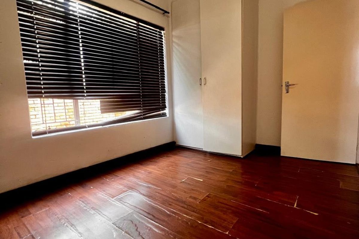 An empty bedroom featuring laminate flooring, a built-in wardrobe, and venetian blinds. The room requires minor repairs to the flooring and window treatments.