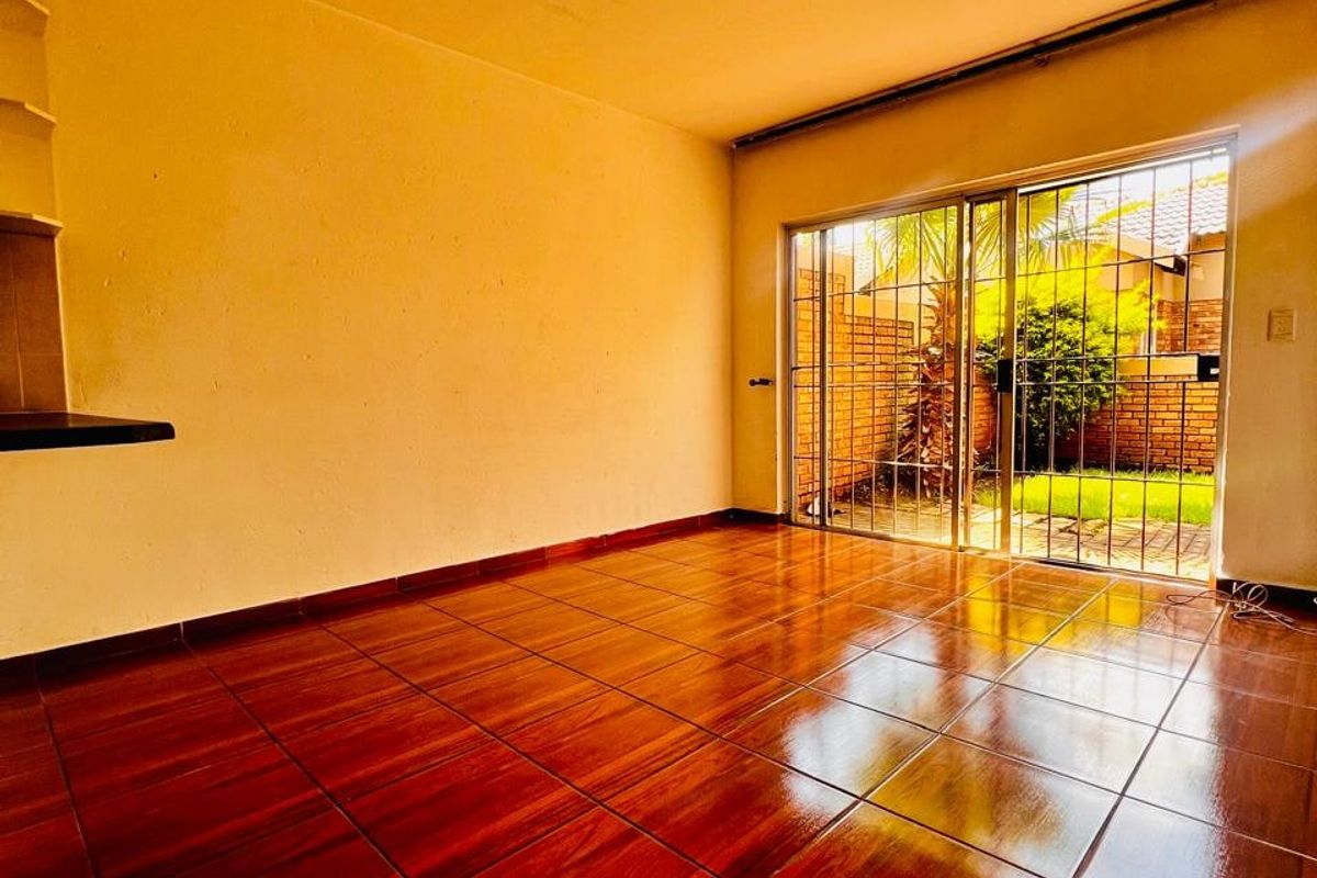 An empty living room featuring polished wood-look floor tiles, built-in shelving, and a sliding glass door providing access to the rear garden area.