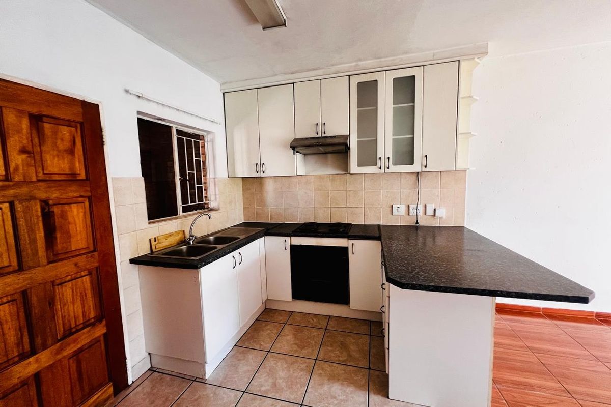 A functional kitchen featuring white cabinetry, dark laminate countertops, a built-in oven with hob, and a breakfast bar, finished with tiled flooring and backsplash.