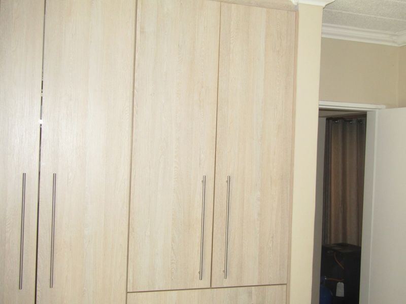 A bedroom featuring light wood-grain built-in cupboards with modern metal handles and decorative ceiling coving.