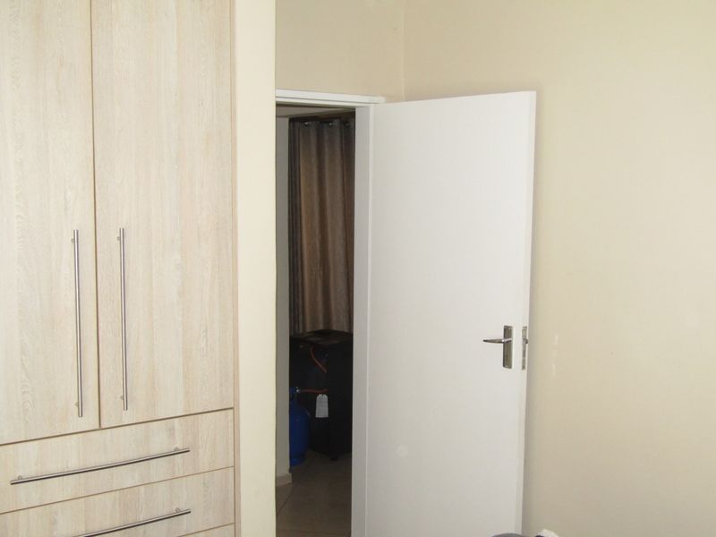 A bedroom interior featuring a light wood-finish built-in wardrobe and a white internal door leading to an adjacent space.