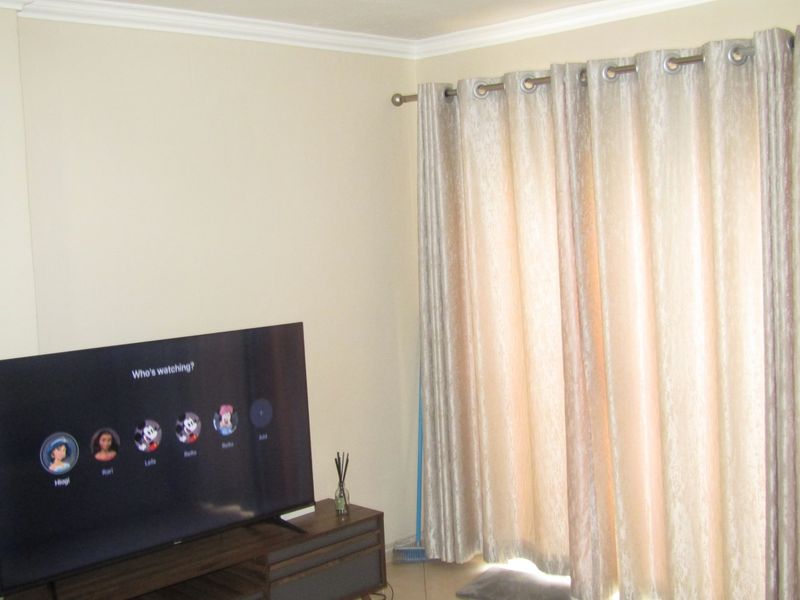 A living room area featuring neutral wall paint, decorative coving, and floor-to-ceiling curtains.