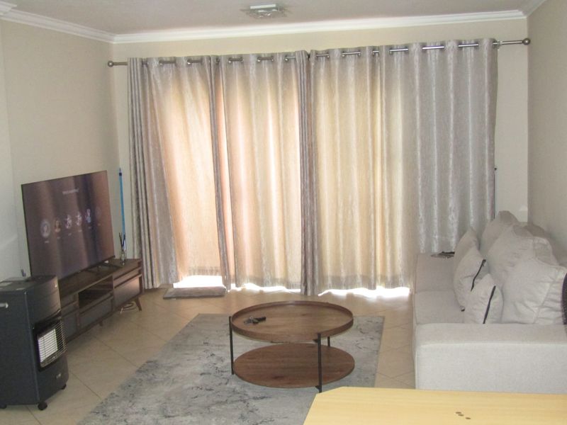A comfortable living room featuring tiled flooring and a large sliding glass door with curtains, providing access to the outdoor area.