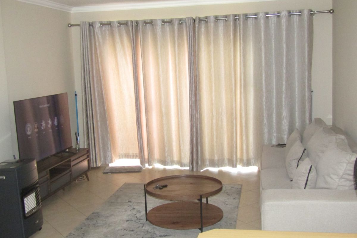 A comfortable living room featuring tiled flooring and a large sliding glass door with curtains, providing access to the outdoor area.
