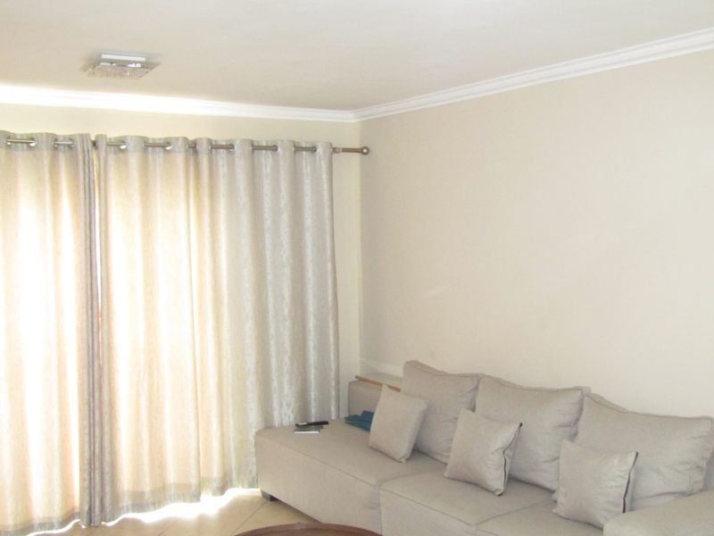 A neutral-toned living room featuring ceiling cornicing and a large window dressed with curtains, providing a bright and simple space.