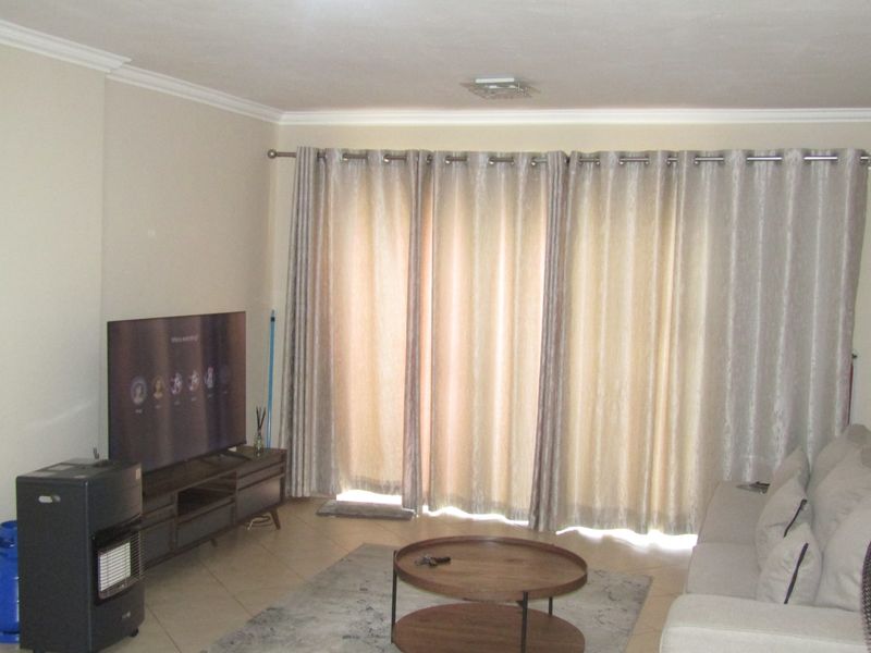 A living room featuring tiled flooring, ceiling cornicing, and a large sliding glass door with floor-to-ceiling curtains.