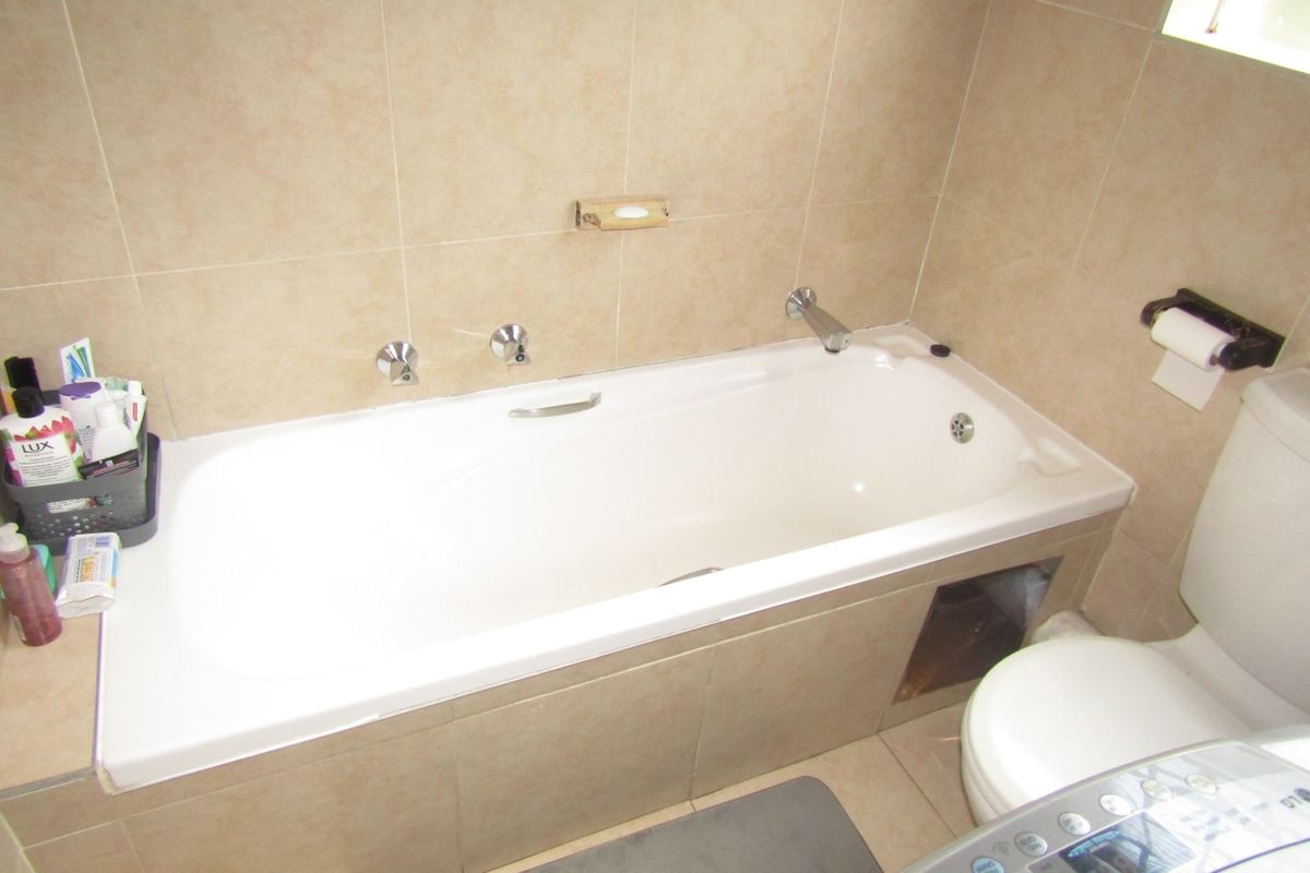 A functional bathroom featuring a built-in bathtub with wall-mounted fixtures and tiled finishes, requiring minor maintenance to the bathtub apron.