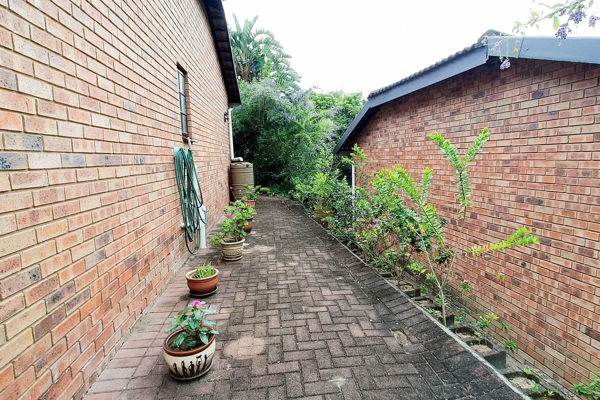A side walkway featuring brick paving between two brick townhouse walls, leading towards a rear garden area with a water tank.
