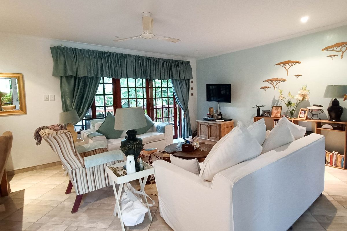 A spacious living room featuring tiled flooring, a ceiling fan, and large french doors that provide access to the outdoor area.