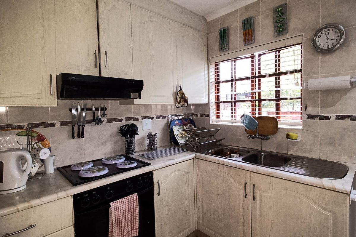 A functional kitchen featuring built-in cabinetry, laminate countertops, a stainless steel double sink, and integrated cooking appliances with a tiled backsplash.