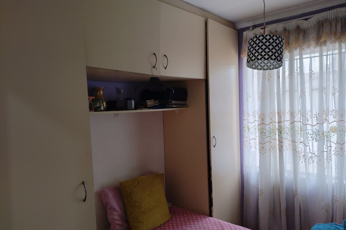 A compact bedroom featuring built-in cupboards with overhead storage and a window fitted with security bars.