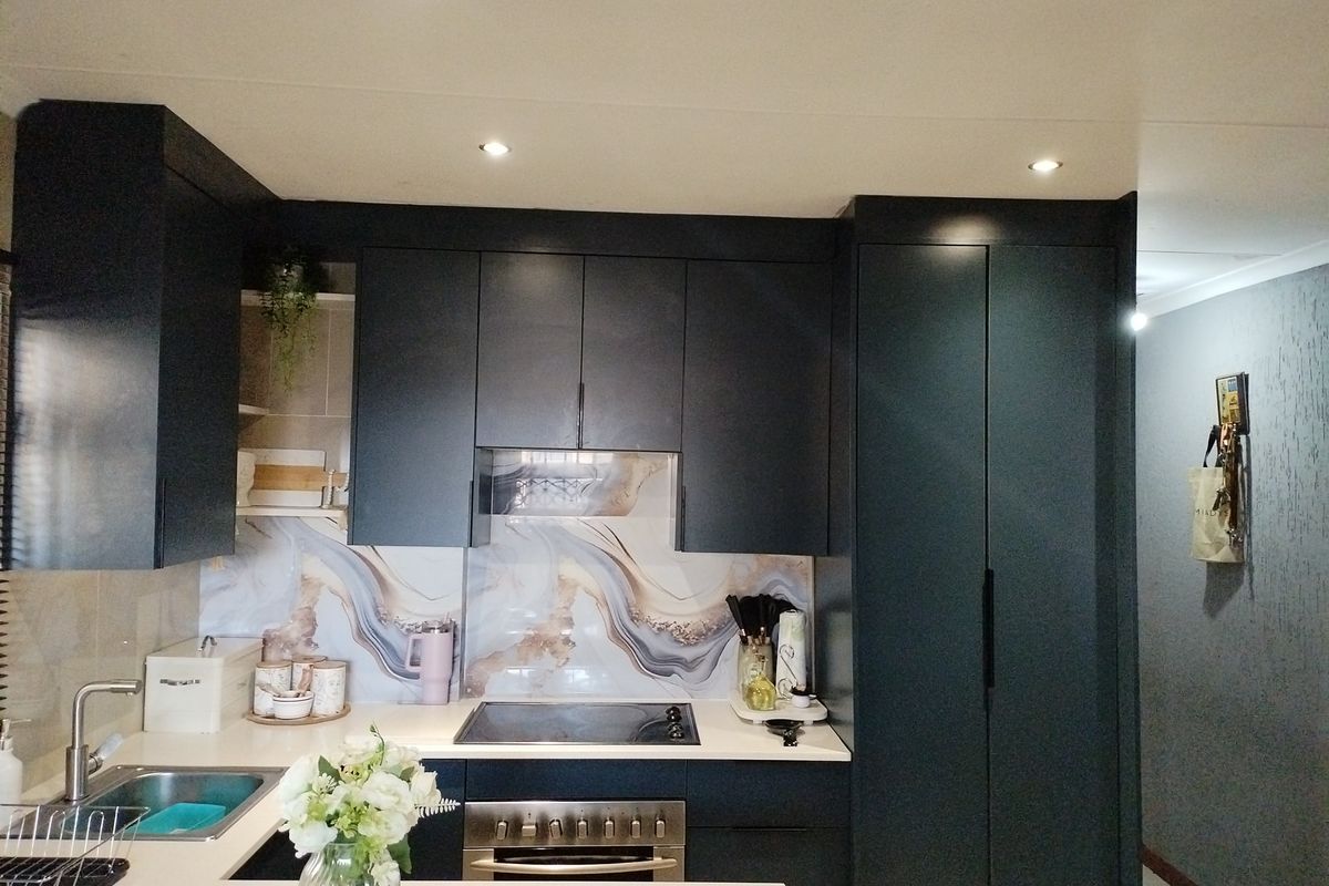 Modern kitchen featuring dark cabinetry, stone countertops, a decorative splashback, and integrated appliances including a hob and oven.