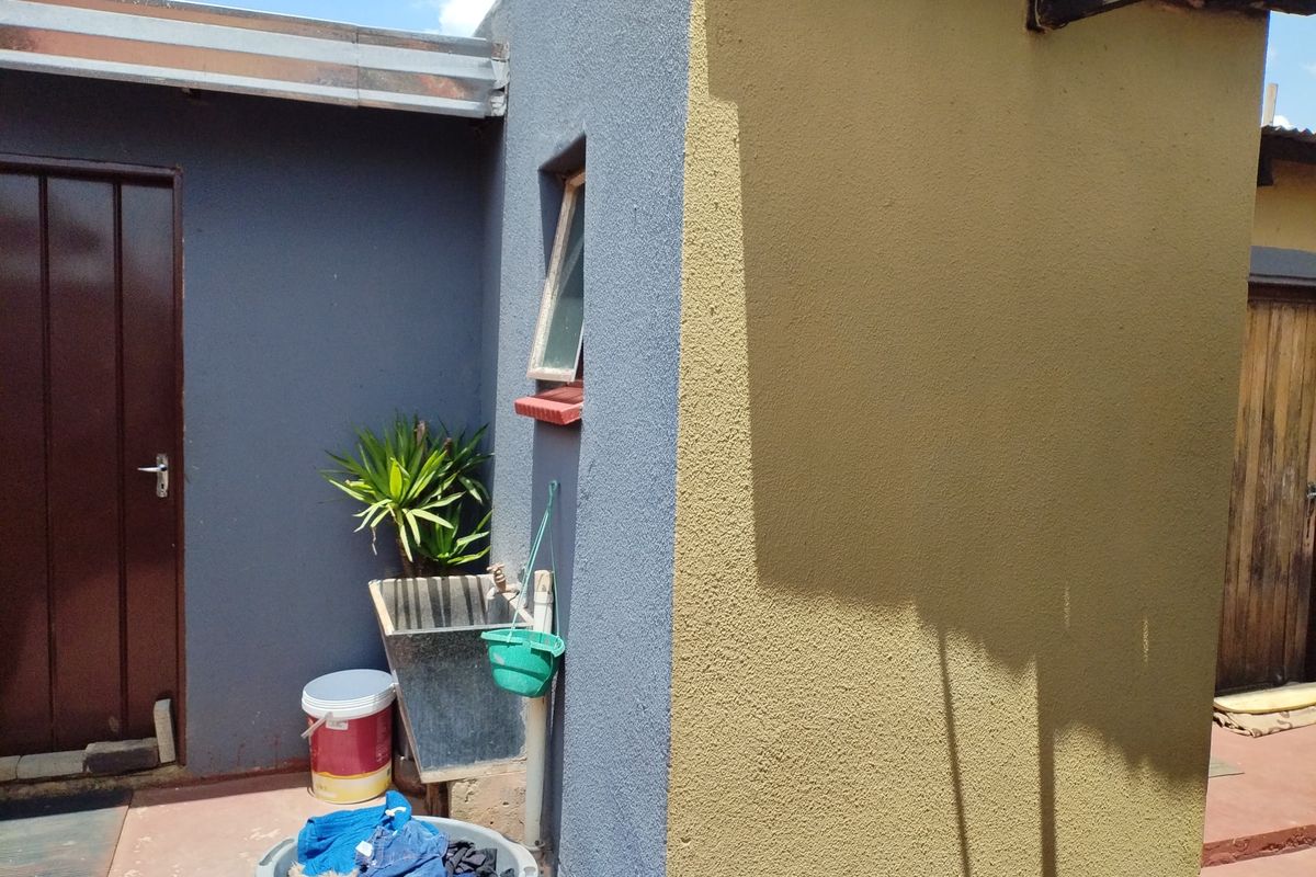 Rear exterior area featuring a utility wash basin, paved patio space, and painted exterior walls with visible wear.