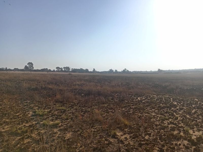 A wide-angle view of a vacant residential plot featuring dry, natural vegetation and open land, suitable for future development.